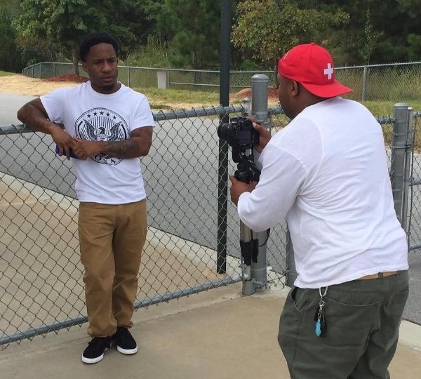 A photographer filming a subject beside a fence on an outdoor location