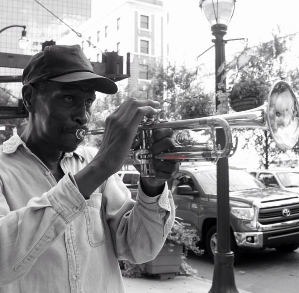 Black-and-white street portrait of a trumpet player performing outdoors