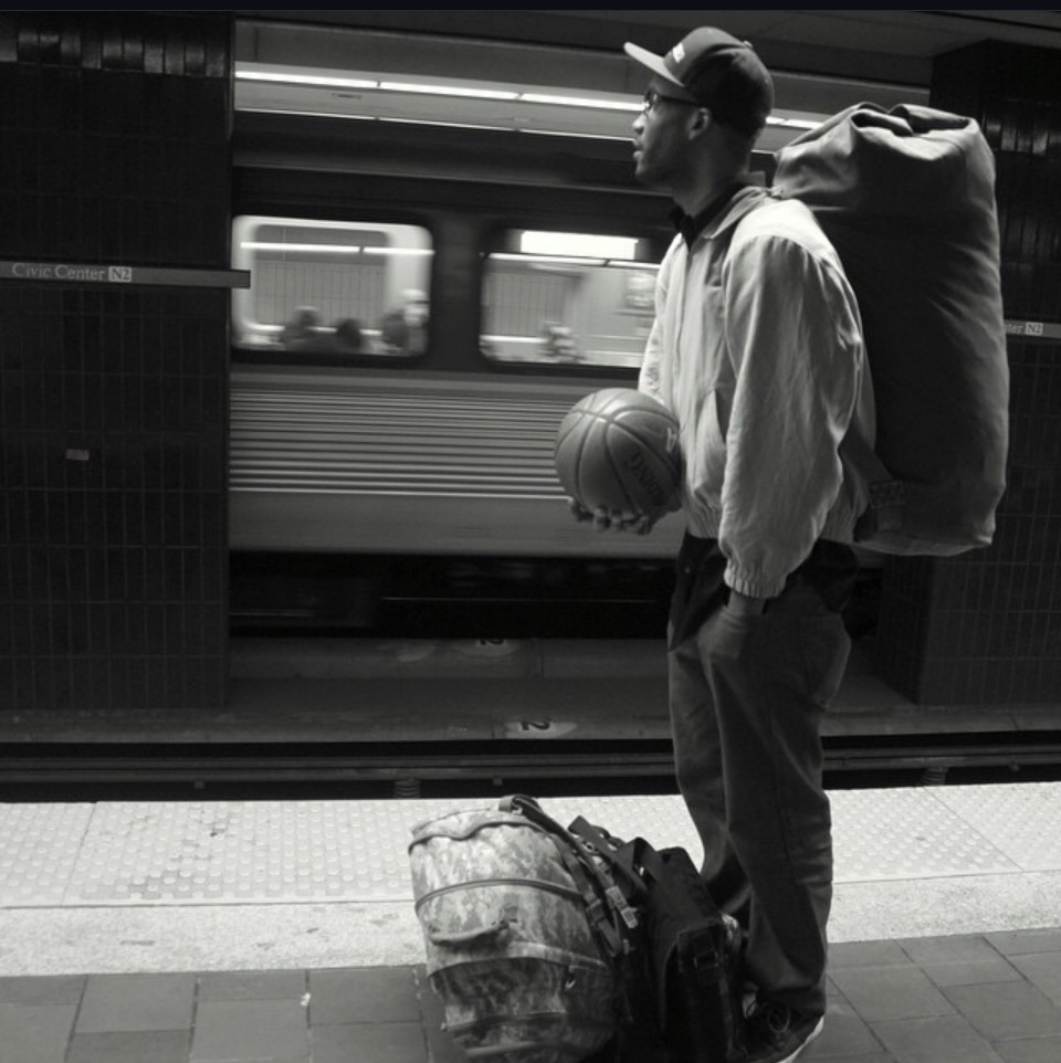Black-and-white portrait of a traveler holding a basketball on a train platform